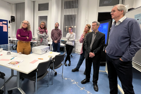 Sieben Personen stehen in einem Raum und gucken an eine Tafel